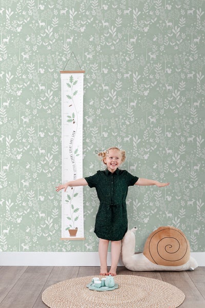 Szene mit einem Kind vor einer bedruckten Tapete, einer Wachstumstabelle und einem Schneckenkuscheltier