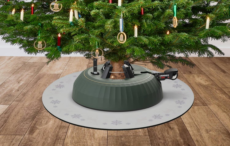 Krinner Christbaumständer unter einem geschmückten Weihnachtsbaum auf einer hellen Unterlage mit Schneeflocken auf einem Holzboden.