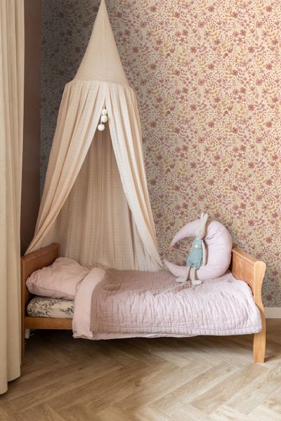 Ein Kinderzimmer mit Himmelbett, blumiger Tapete und einem Holzfußboden.