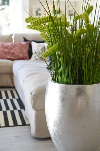 Künstliches Ziergras in einer Bodenvase in einem modern eingerichteten Wohnzimmer mit Sofa und gestreiftem Teppich.