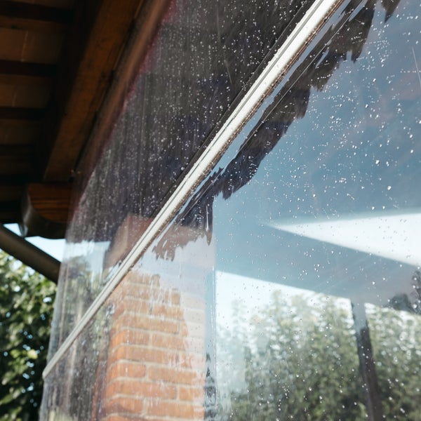 Transparenter Wetterschutzvorhang für Terrassen mit Regentropfen und Reißverschluss an einer Holzkonstruktion.