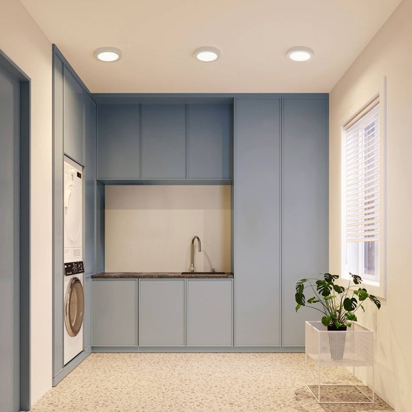 Moderner, heller Hauswirtschaftsraum mit blauen Einbauschränken, integrierter Waschmaschine und Trockner sowie drei runden Deckeneinbauleuchten.