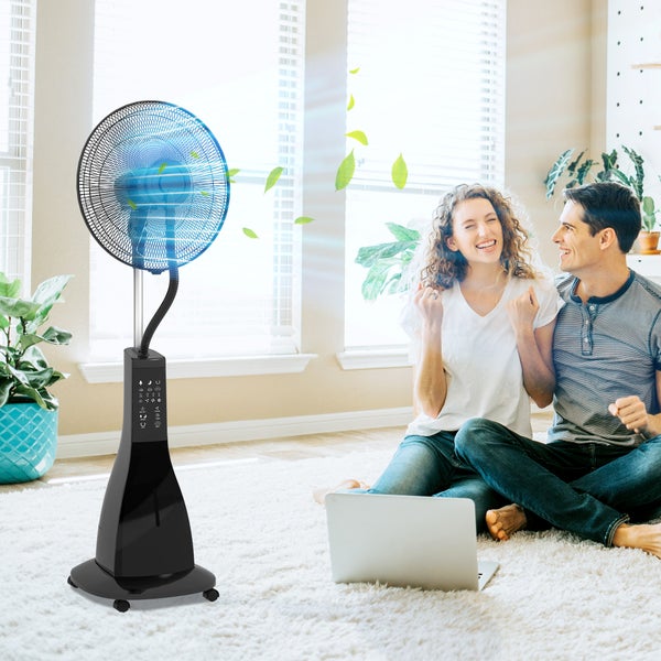 Ein schwarzer Standventilator mit Sprühnebelfunktion sorgt in einem hellen Wohnzimmer für Abkühlung bei einem Paar, das auf einem Teppich sitzt.