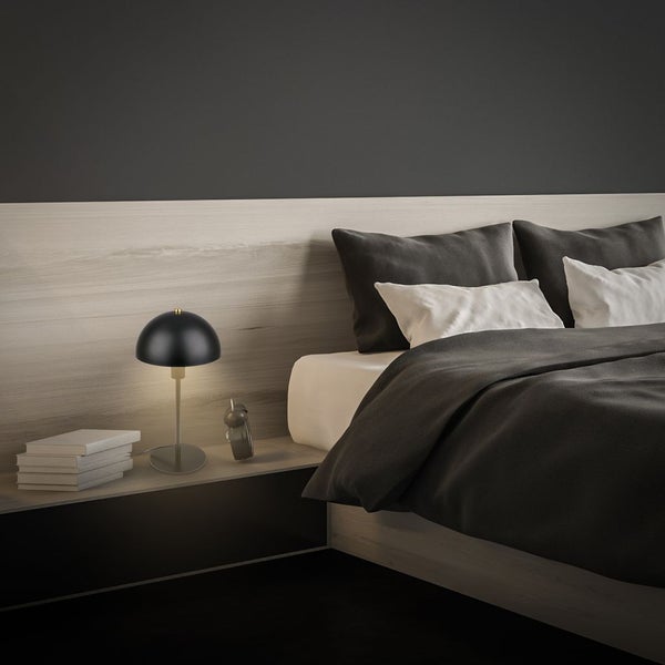 Moderne Tischleuchte mit schwarzem, halbkugelförmigem Schirm auf einem Nachttisch in einem minimalistischen Schlafzimmer.