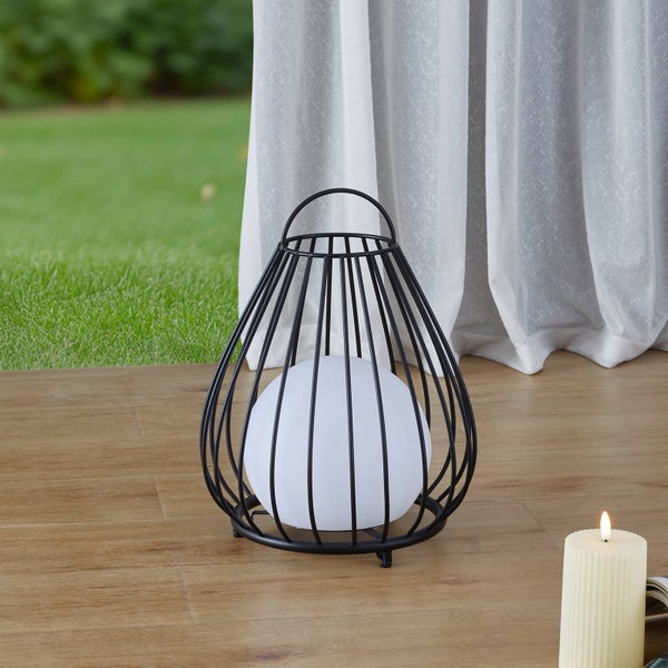 Moderne dekorative Außenleuchte in Käfigform aus schwarzem Metall mit weißer Lichtkugel auf einer hellen Holzterrasse.