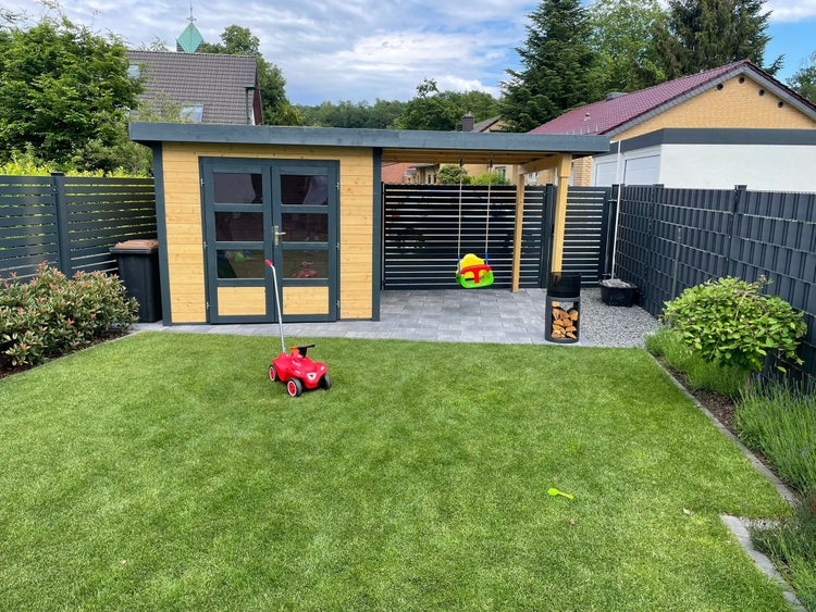 Modernes Gartenhaus aus Holz mit Flachdach, Doppeltür, integriertem Schleppdach mit Schaukel, Rasenfläche und Sichtschutzzaun.