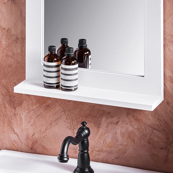 Detailansicht eines Badezimmers mit Spiegel, Ablage und Kosmetikprodukten sowie einem Wasserhahn.