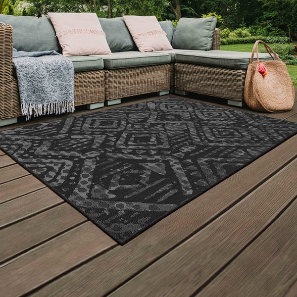 Outdoor-Teppich mit geometrischem Muster auf einer Holzterrasse mit Lounge-Möbeln aus Geflecht und Kissen.