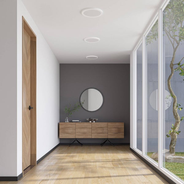Moderner Flur mit Holzboden, einem Sideboard, einem runden Spiegel an einer grauen Wand und drei runden Einbauleuchten neben großen Fenstern.
