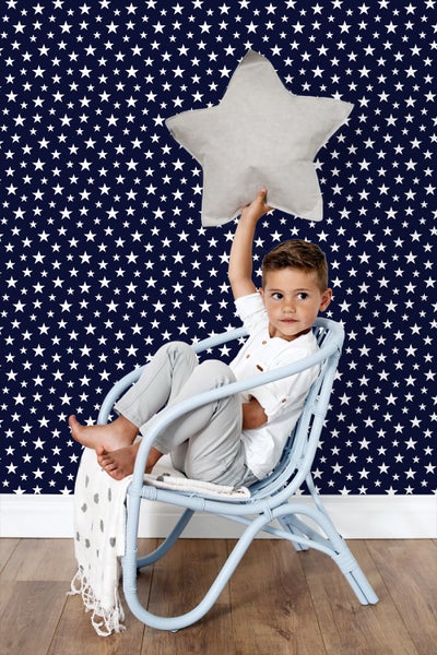 Kind sitzt in einem Rattansessel vor einer Wand mit Sternenmuster und hält ein Sternenkissen.