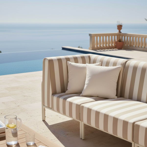 Gestreiftes Outdoor-Sofa mit zwei Kissen auf einer hellen Steinterrasse neben einem Pool mit Blick auf das Meer.