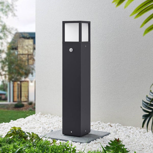 Rechteckige Wegeleuchte mit integriertem Bewegungsmelder und weißem Diffusor, platziert auf weißen Kieselsteinen vor einer hellen Wand im Garten.