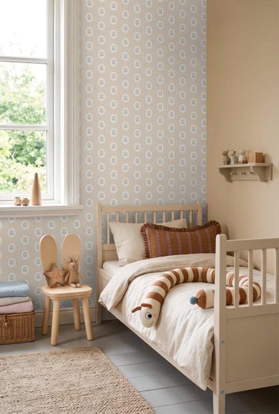 Hell gestaltetes Kinderzimmer mit einer Tapete mit Streifen und Blumenmotiven, einem Bett aus hellem Holz und einem Hasenohren-Stuhl.