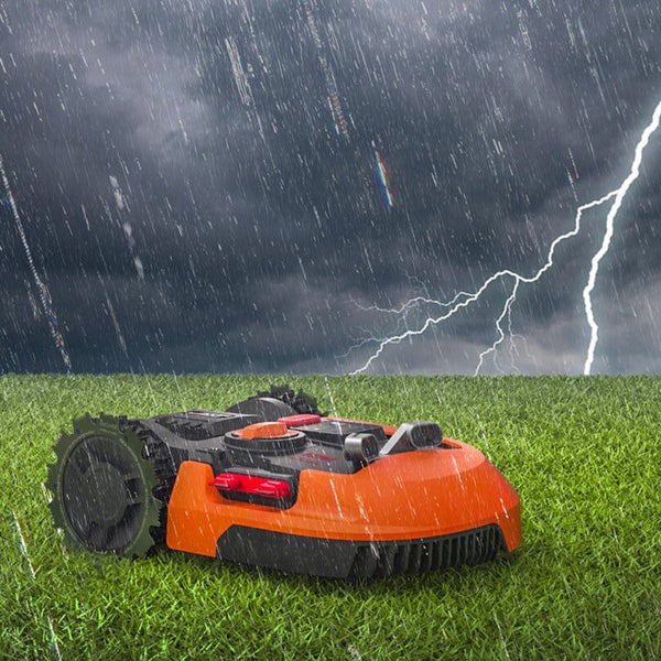 Ein Rasenmähroboter steht bei Regen und Gewitter auf einer Wiese.
