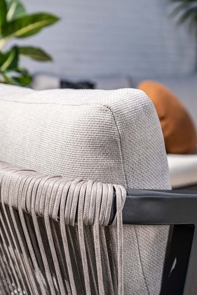 Nahaufnahme eines Gartenstuhls mit strukturiertem Stoffkissen und dekorativer Seilbespannung an einem dunklen Rahmen.