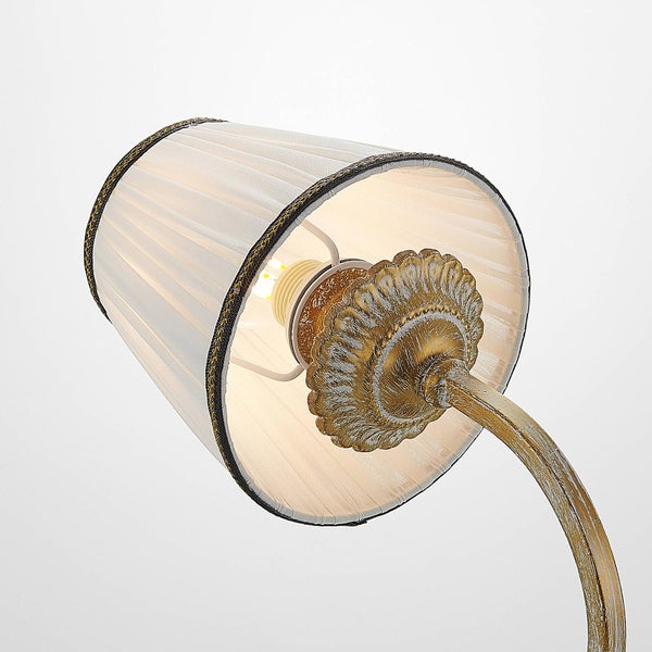 Nahaufnahme einer klassischen Leuchte mit plissiertem Stoffschirm und Metallelement in Antikgold.