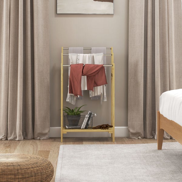 Kleiderständer aus Bambus mit drei Metallstangen und Ablage in einem hellen Schlafzimmer zwischen Vorhängen.