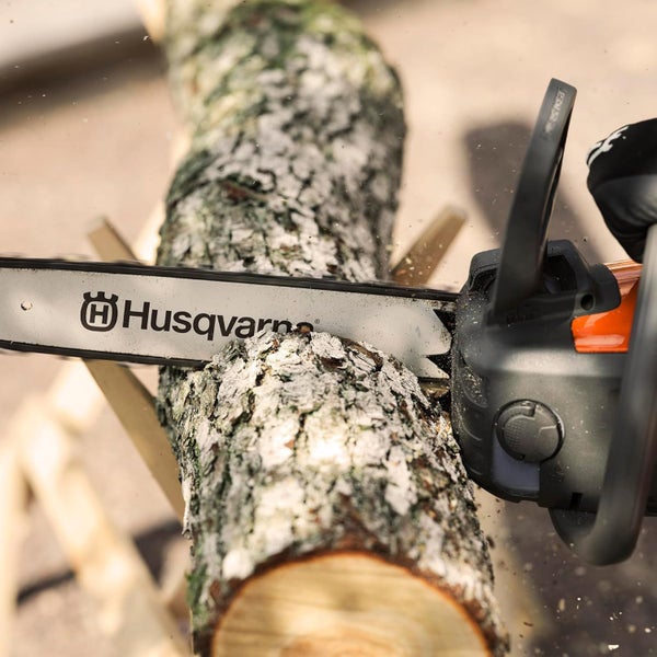 Eine Husqvarna Kettensäge beim Zersägen eines Baumstammes auf einem Sägebock.