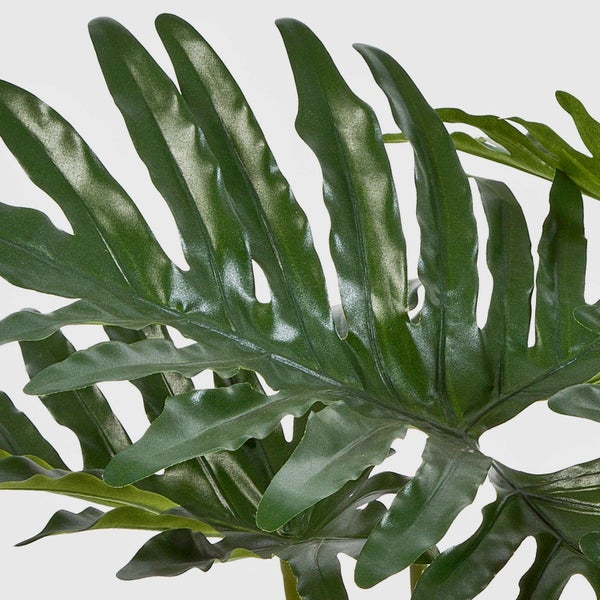 Künstliche Philodendron-Pflanze mit großen gelappten Blättern und dicken grünen Stielen in einem schwarzen Topf.