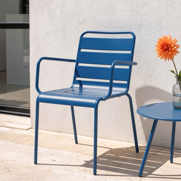 Moderner blauer Gartenstuhl aus Metall mit Armlehnen und passendem runden Beistelltisch auf einer hellen Steinterrasse.