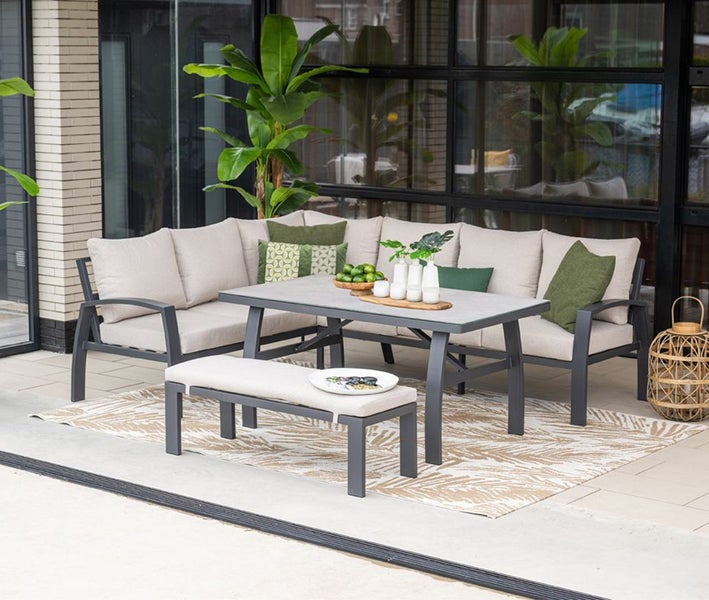 L-förmiges Garten-Lounge-Set mit Tisch, Bank und Sitzpolstern auf einer Terrasse. Metallrahmen, organisierte und helle Atmosphäre.