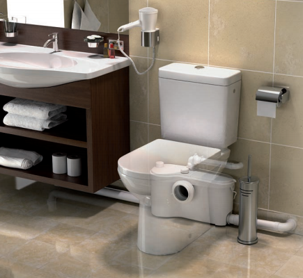 Kleinhebeanlage für Toilette und Waschbecken, installiert hinter einer Toilette in einem modernen Badezimmer mit dunklem Waschtisch.