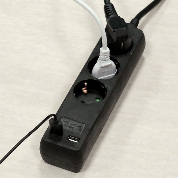 Schwarze Steckdosenleiste mit drei Steckplätzen und zwei USB-Anschlüssen sowie eingesteckten Steckern und einem USB-Kabel.