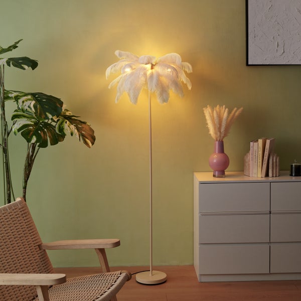 Stehlampe mit Federschirm in Palmenoptik in einem Wohnzimmer mit Sessel, Zimmerpflanze und Kommode.