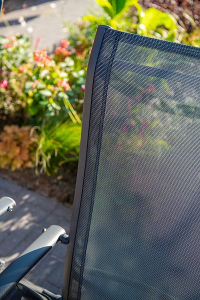Detailaufnahme der Rückenlehne eines Gartenstuhls aus feinem Netzgewebe mit einem dunklen Metallrahmen im Garten.