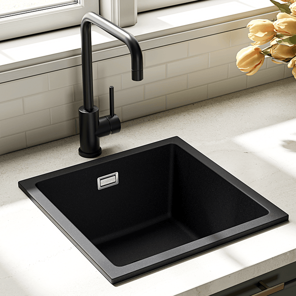 Quadratisches Spülbecken aus Granitverbundstoff mit schwarzer Küchenarmatur in einer modernen Küche mit beigefarbener Arbeitsplatte.