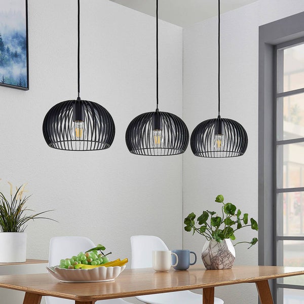 Drei schwarze Pendelleuchten mit Edison-Glühbirnen über einem Holztisch in einem hellen Raum.