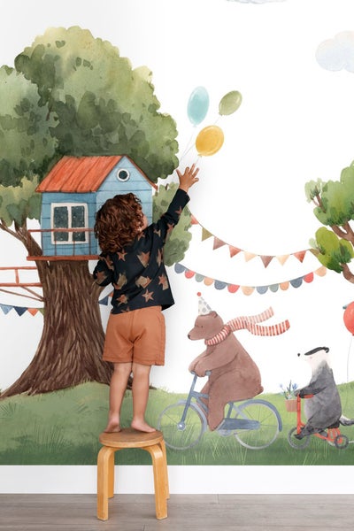 Illustration einer Wandtapete mit einem Baumhaus, einem Jungen, der nach Luftballons greift, und Tieren auf Fahrrädern