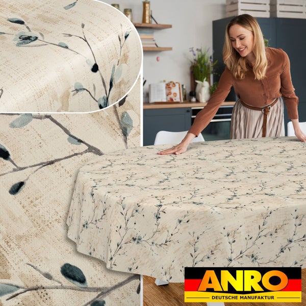 Frau breitet abwaschbare Tischdecke mit Astmuster auf einem runden Tisch in einer hellen Küche aus. ANRO Deutsche Manufaktur Logo.