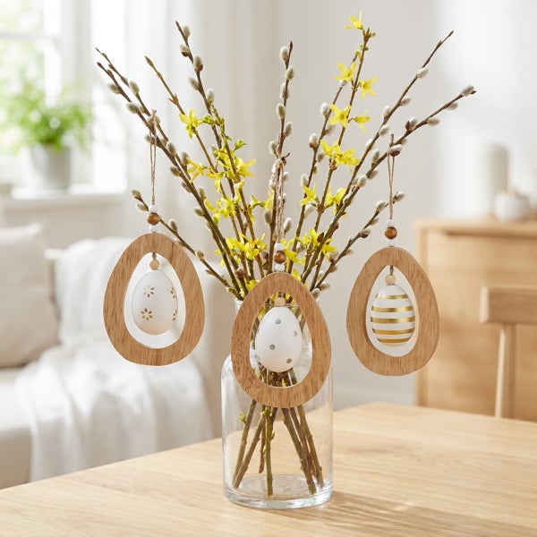 Osterstrauß in Glasvase mit drei hängenden Holzelementen und Ostereiern als Dekoration für den Frühling