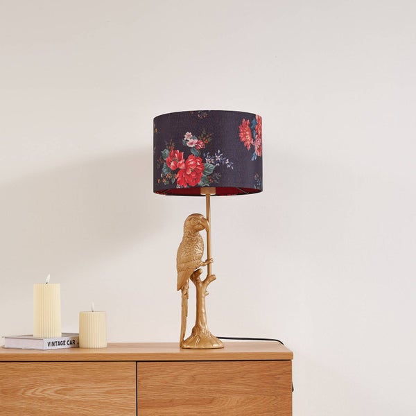 Dekorative Tischleuchte mit Papageienfuß und floralem Lampenschirm auf einer Holzkommode