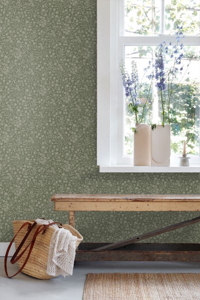 Vliestapete mit feinem Blumenmuster auf grünem Grund in einem hellen Zimmer mit einer rustikalen Holzbank und einem Fenster.