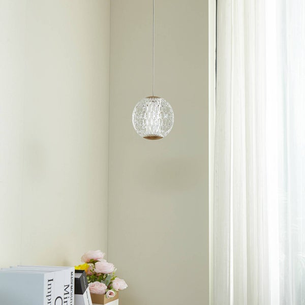 Moderne Pendelleuchte mit kugelförmigem Glasschirm in Kristall-Optik, aufgehängt in einem hellen, minimalistischen Raum neben einem Vorhang.
