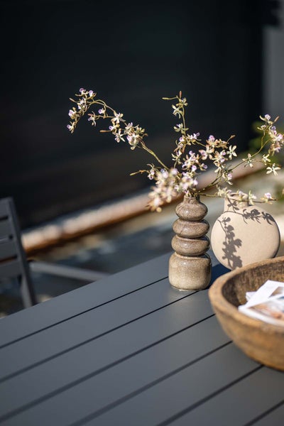 Moderne Tischdekoration mit einer gestuften Keramikvase mit Orchideenzweigen, einer runden Vase und einer Holzschale auf einem Lattentisch.