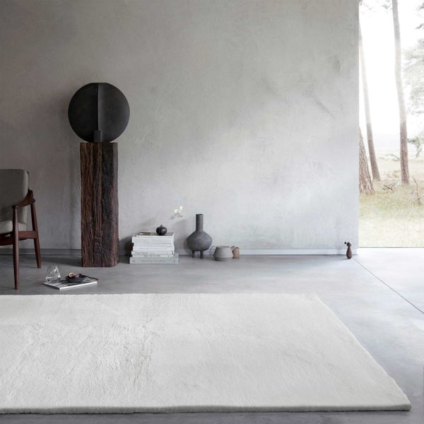 Weißer Hochflor-Teppich in einem hellen, geräumigen Wohnzimmer mit Betonboden und minimalistischem Design.