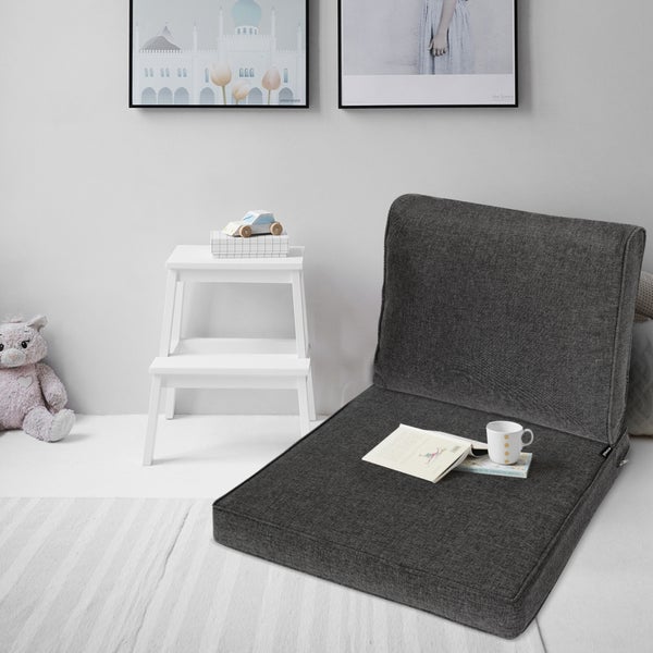 Dunkelgraues Bodensofa aus Stoff in einer hellen Leseecke mit einem Buch, einem weißen Tritthocker und einem Plüschtier.