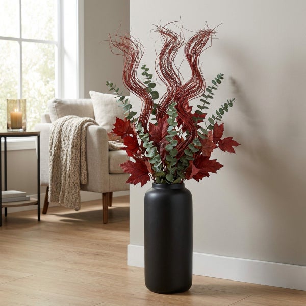 Dekorative Bodenvase in Schwarz mit einem herbstlichen Strauß aus künstlichen Ahornblättern und gewundenen Zweigen im Wohnzimmer.