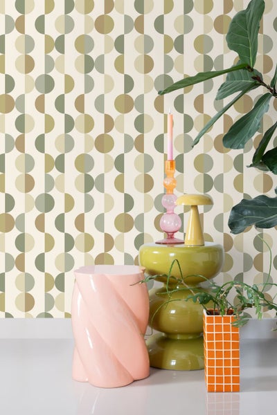 Retro-Einrichtungsszene mit geometrischer Tapete in Erdtönen, einem rosa gedrehten Hocker, olivgrünem Beistelltisch und grünen Zimmerpflanzen.