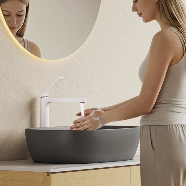 Frau wäscht sich die Hände in einem Badezimmer mit einem grauen Aufsatzwaschbecken und einem weißen Wasserhahn.