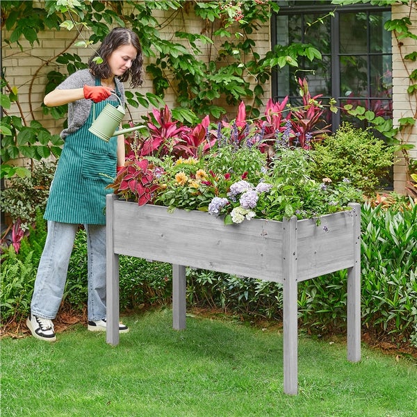 Frau gießt Blumen in einem Hochbeet im Garten.