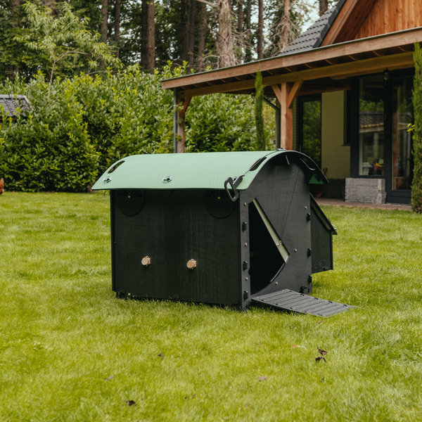 Hühnerstall aus Kunststoff mit grünem Bogendach und Rampe auf einer Rasenfläche im Garten.