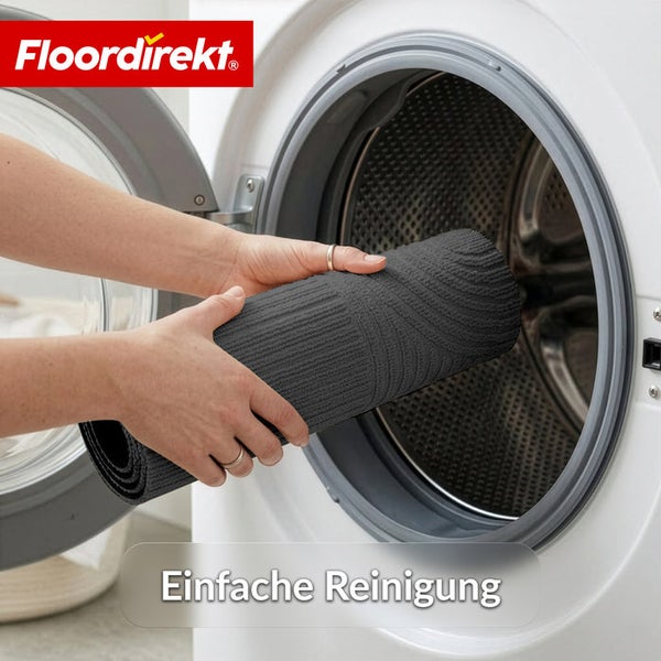Eine Person legt eine gerollte graue Badematte in eine Waschmaschine. Floordirekt Logo. Einfache Reinigung.
