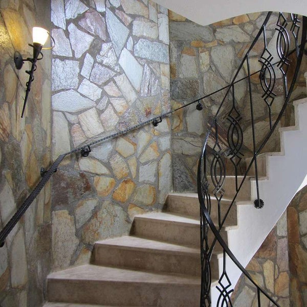 Treppenhaus mit Natursteinwand und Metallgeländer