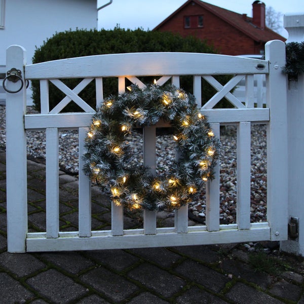 Weihnachtlicher Tannenkranz mit Beleuchtung an einem Gartenzaun