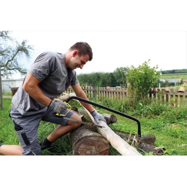 Ein Handwerker sägt mit einer Bügelsäge einen Holzstamm im Garten.