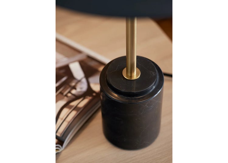 Tischlampe mit zylindrischem Fuß aus Marmor und einem metallenen Ständer auf einem hölzernen Tisch neben einer Zeitschrift.